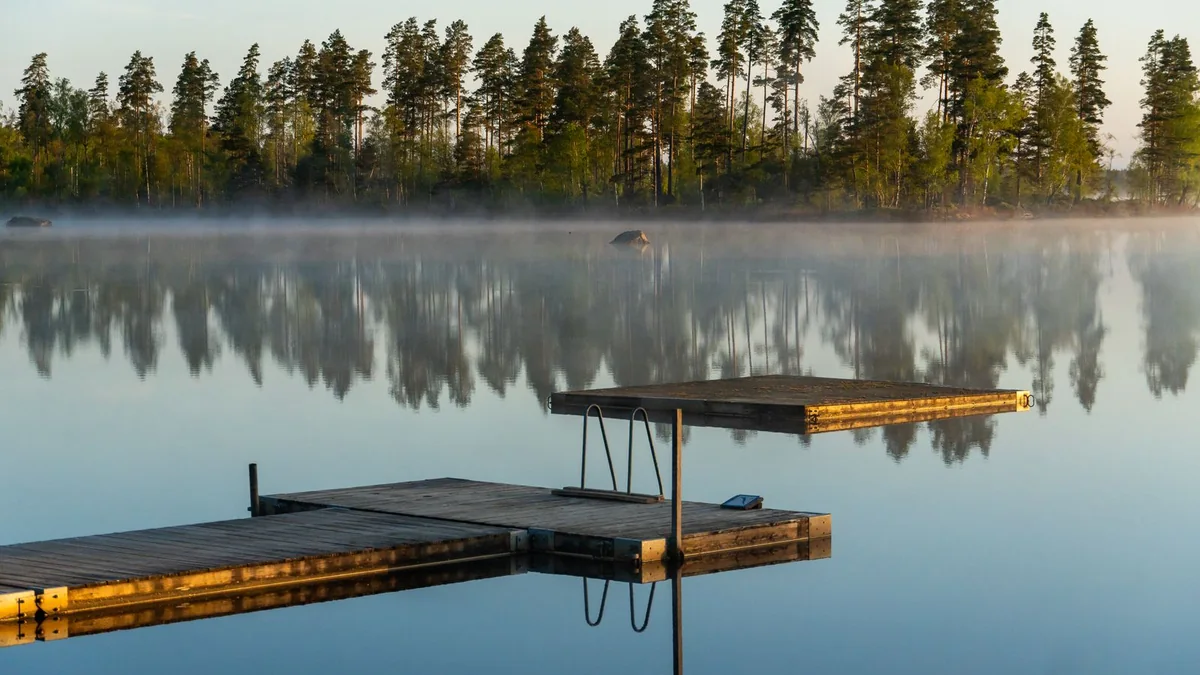 A calm lake at dawn with mist over the water and a wooden dock in the foreground