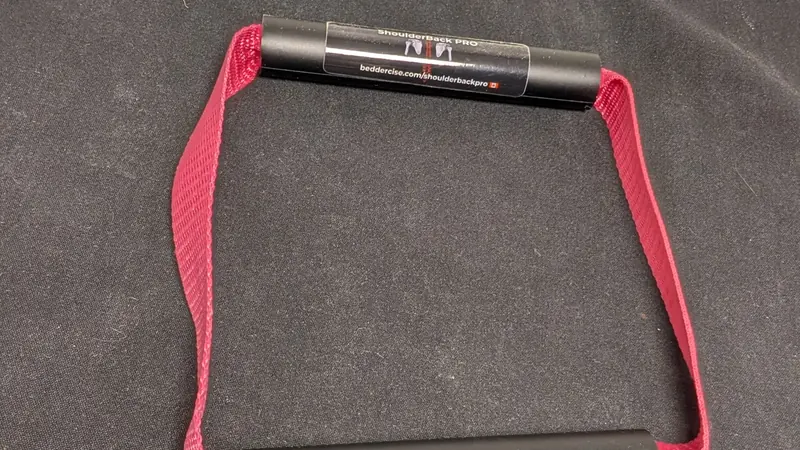 ShoulderBack Pro trainer with a burgundy strap resting on a dark cushion