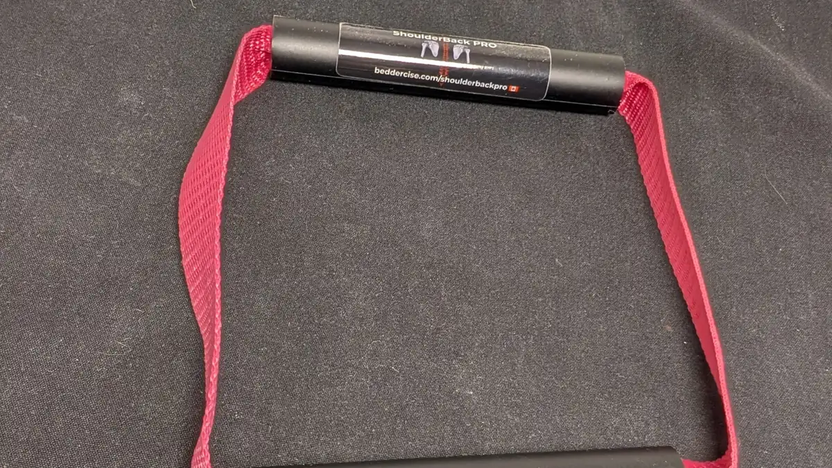 ShoulderBack Pro trainer with a burgundy strap resting on a dark cushion